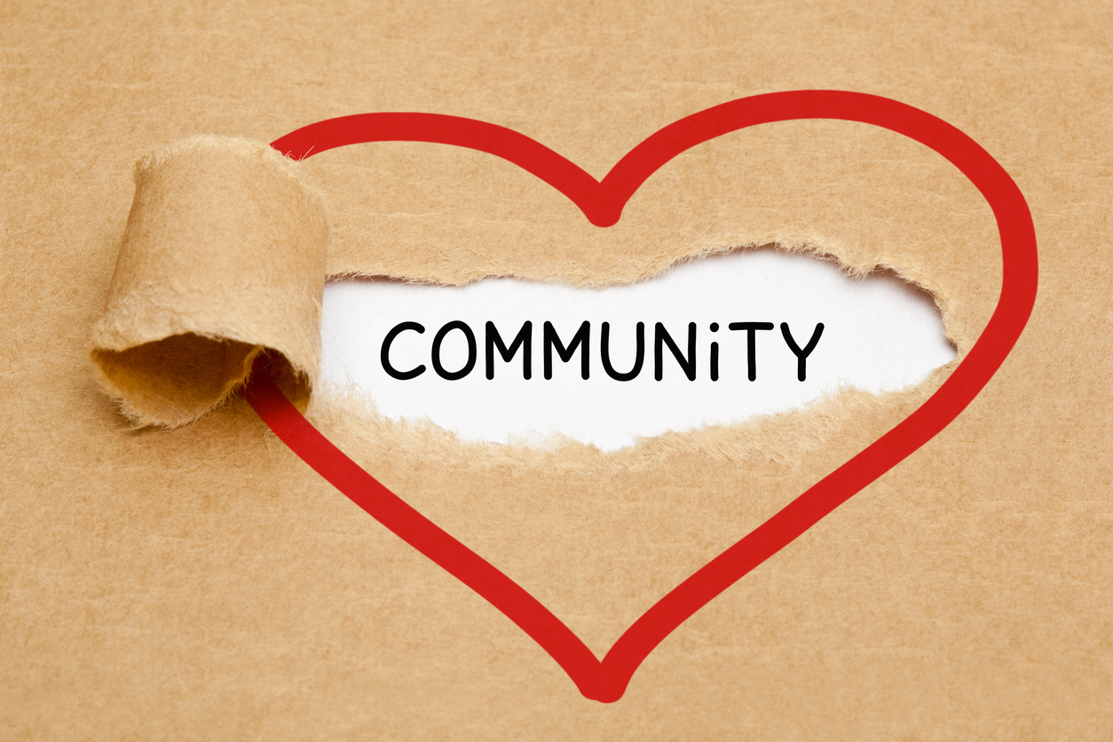 Handwritten word Community appearing behind torn red heart on brown paper.